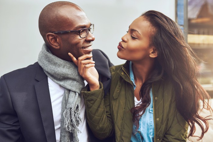 Flirting young African American woman pursing her lips for a kiss and caressing the face of a handsome man in glasses as they enjoy a date together