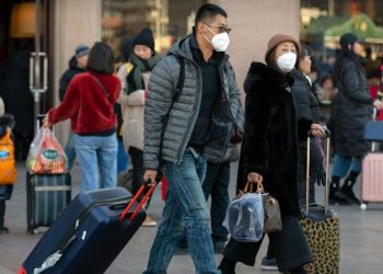 Travelers wear face masks as they walk outside of the Beijing Railway Station in Beijing, Monday, Jan. 20, 2020. China reported Monday a sharp rise in the number of people infected with a new coronavirus, including the first cases in the capital. The outbreak coincides with the country's busiest travel period, as millions board trains and planes for the Lunar New Year holidays. (AP Photo/Mark Schiefelbein)
