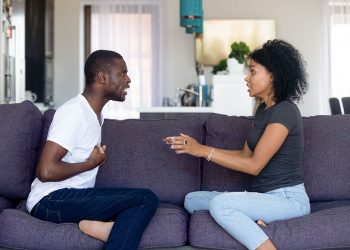 Unhappy African American couple quarreling, sitting on sofa at home, upset woman shouting, blaming black man, emotionally arguing, family conflict between wife and husband, break up