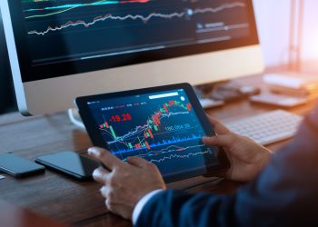 Businessman checking stock market on digital tablet and a desktop computer with stock exchange graph on screen. Financial stock market. Analyzing data in office background.